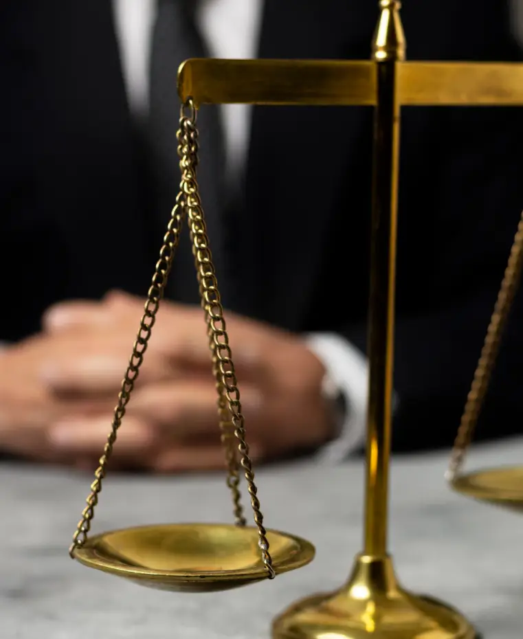 A close-up of a gold balance scale with a person's hands clasped in the background, symbolizing justice and law