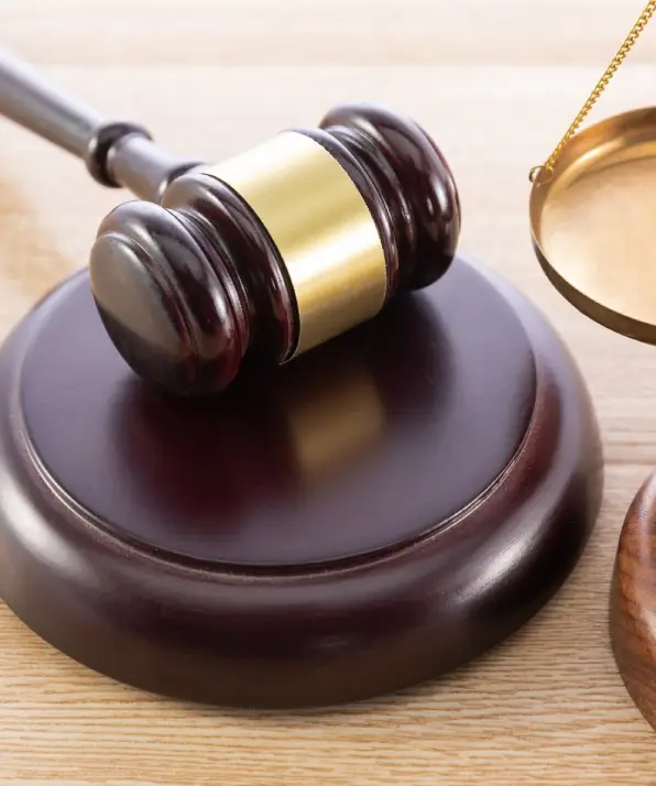 A wooden gavel rests on a circular base, beside a brass scale, symbolizing justice and law